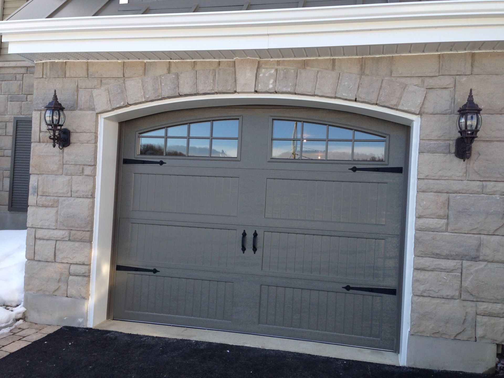 Grey garage door with arched windows and black hardware in a stone facade