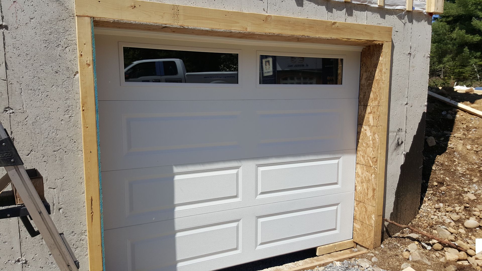 Light-coloured garage door with two windows in a timber frame on a construction site