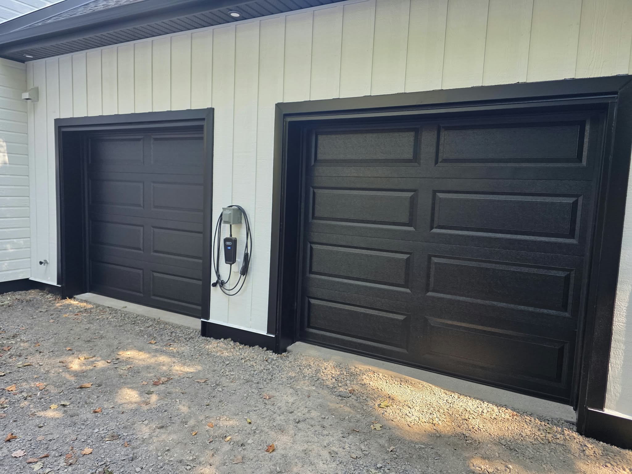 Two black panelled garage doors in a white exterior wall